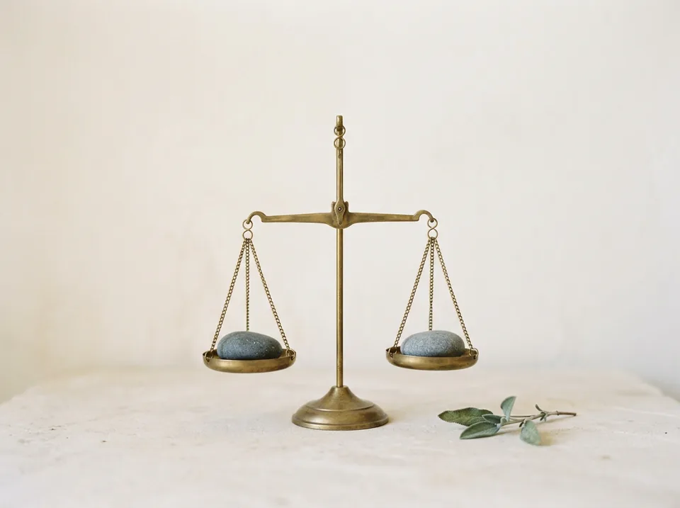 A brass balance scale holding one pebble in each pan, level.